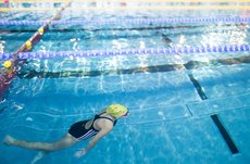 Foto einer Frau, die entlang der Bahn eines Schwimmbeckens taucht. 