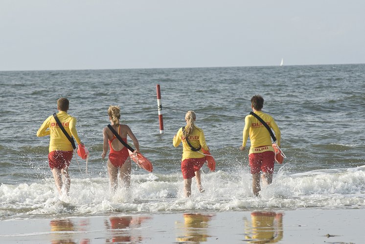 Rettungsschwimmer laufen mit Rettungsgerät ins Meer.