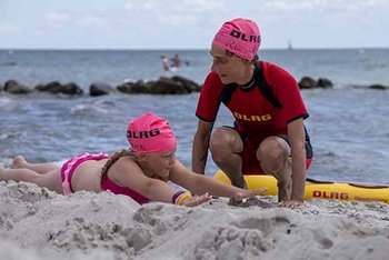 Kind streckt Arme und Beine mit Ausbilderin am Strand