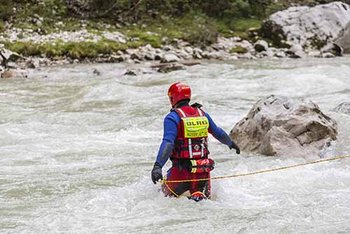 Strömungsretter in rot-blauer Einsatzkleidung (von hinten) geht mit Rettungsleine in fließendes Gewässer